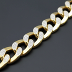 A close-up of a gold Cuban link chain bracelet with clear pavé-set stones on the front of each link, photographed on a dark gray background.