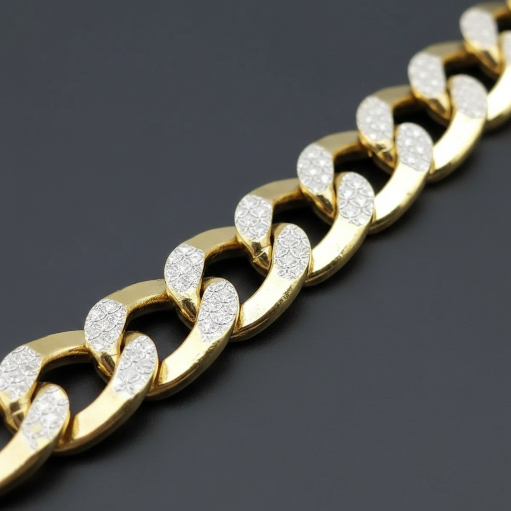 A close-up of a gold Cuban link chain bracelet with clear pavé-set stones on the front of each link, photographed on a dark gray background.