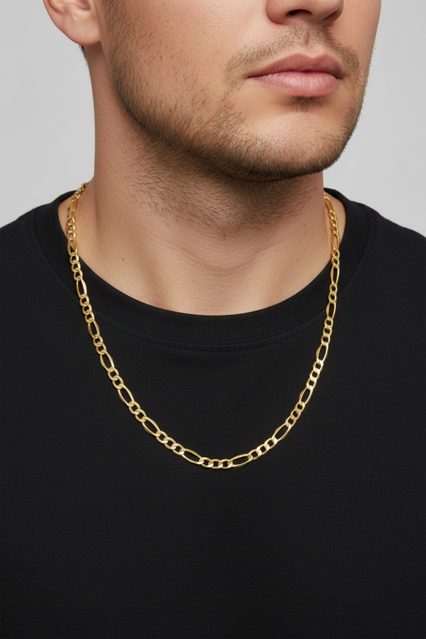A close-up of a man wearing a gold Figaro chain necklace over a black t-shirt, against a neutral gray background.