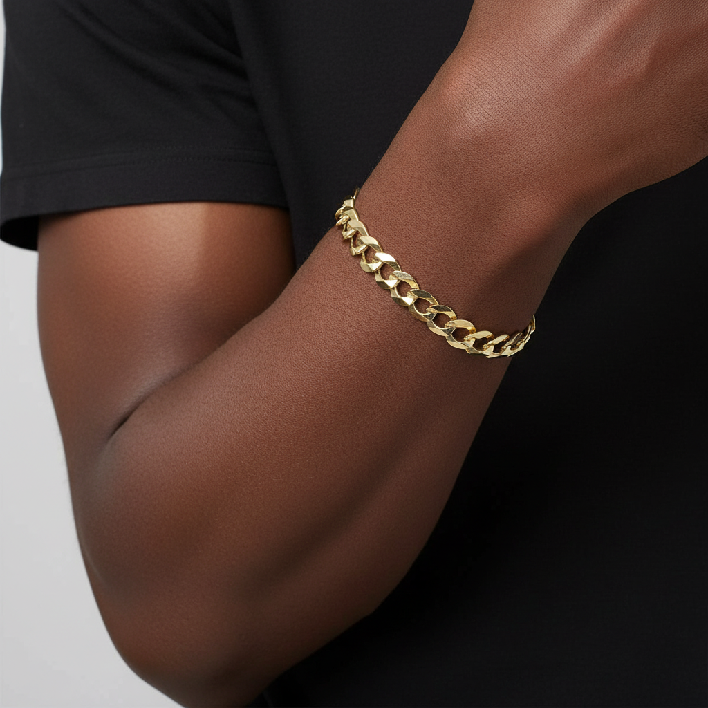 A close-up of a person's forearm wearing a polished gold Cuban link chain bracelet against a black shirt and light gray background.