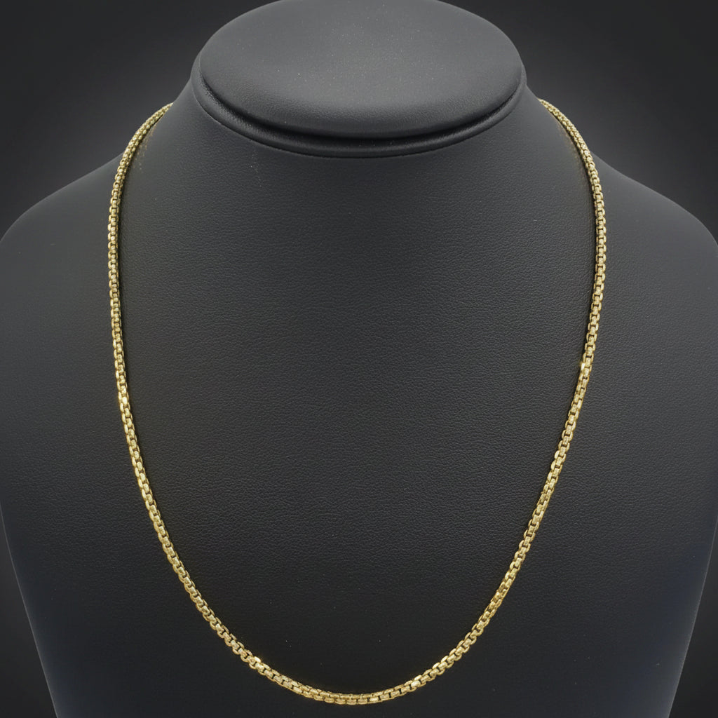 A gold chain necklace displayed on a black jewelry bust against a dark gray gradient background.