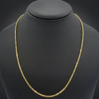 A gold chain necklace displayed on a black jewelry bust against a dark gray gradient background.