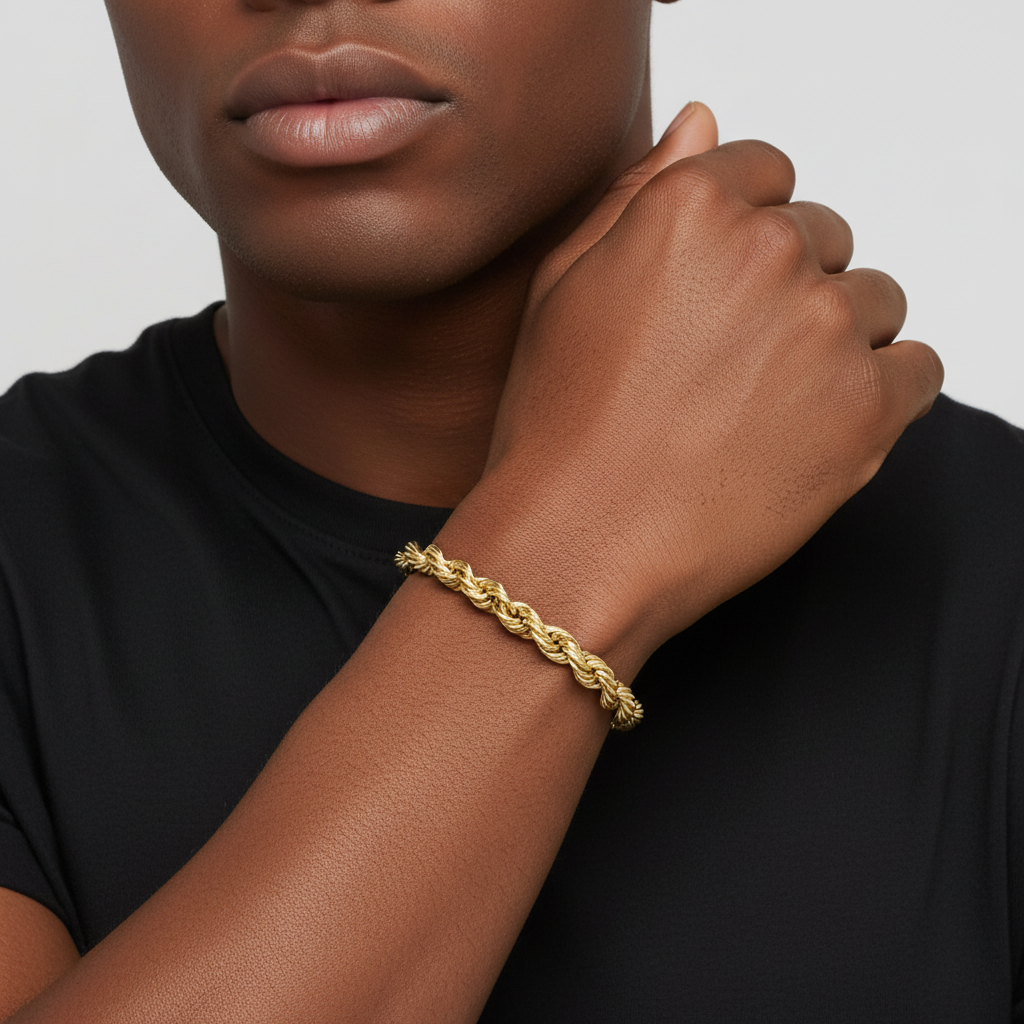 A close-up of a person wearing a gold chain link bracelet on their wrist, dressed in a black t-shirt against a light gray background.