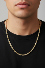 A close-up of a man wearing a twisted gold chain necklace over a black t-shirt, set against a neutral gray background.