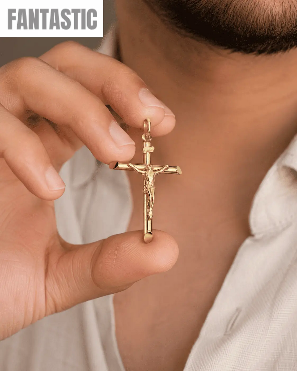 Gold crucifix pendant held by a hand against a neutral background