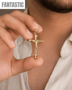 Gold crucifix pendant held by a hand against a neutral background