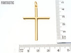 Gold cross pendant with a ruler for scale on a white background