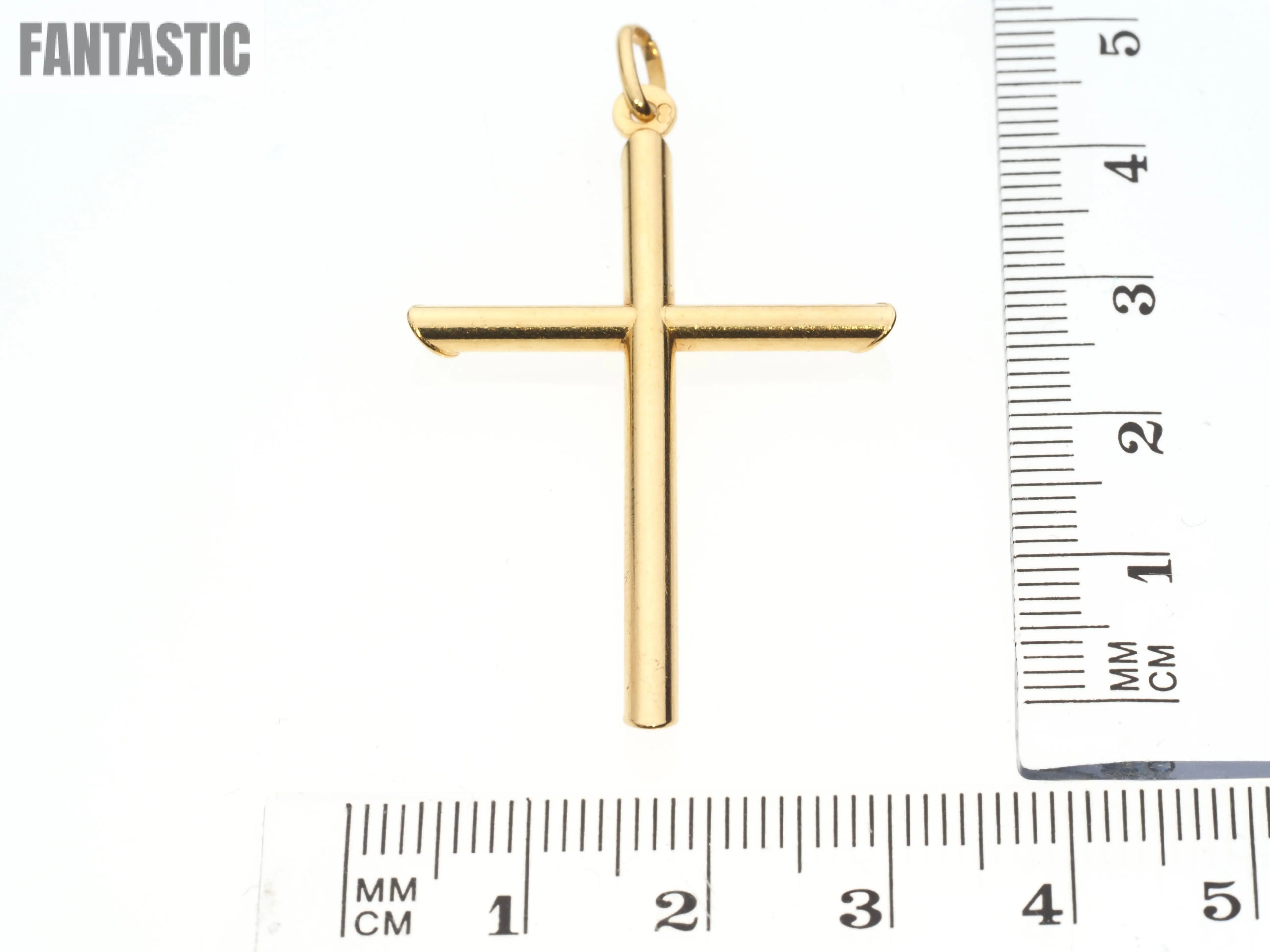 Gold cross pendant with a ruler for scale on a white background