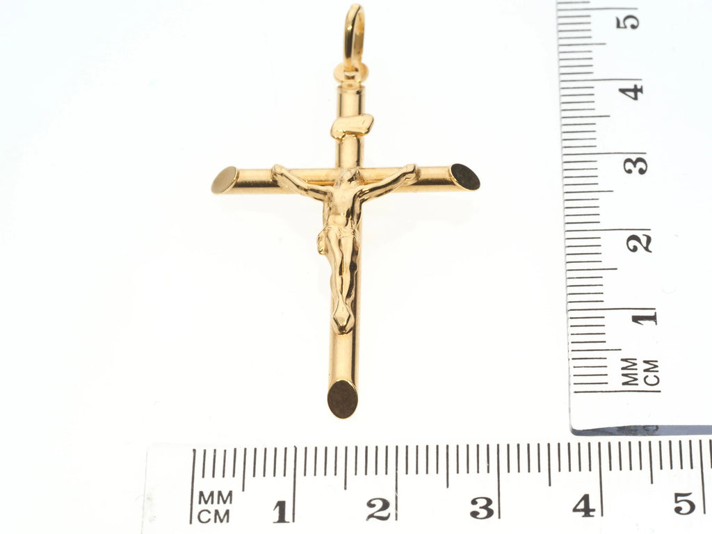 Gold crucifix pendant with a ruler for scale on a white background
