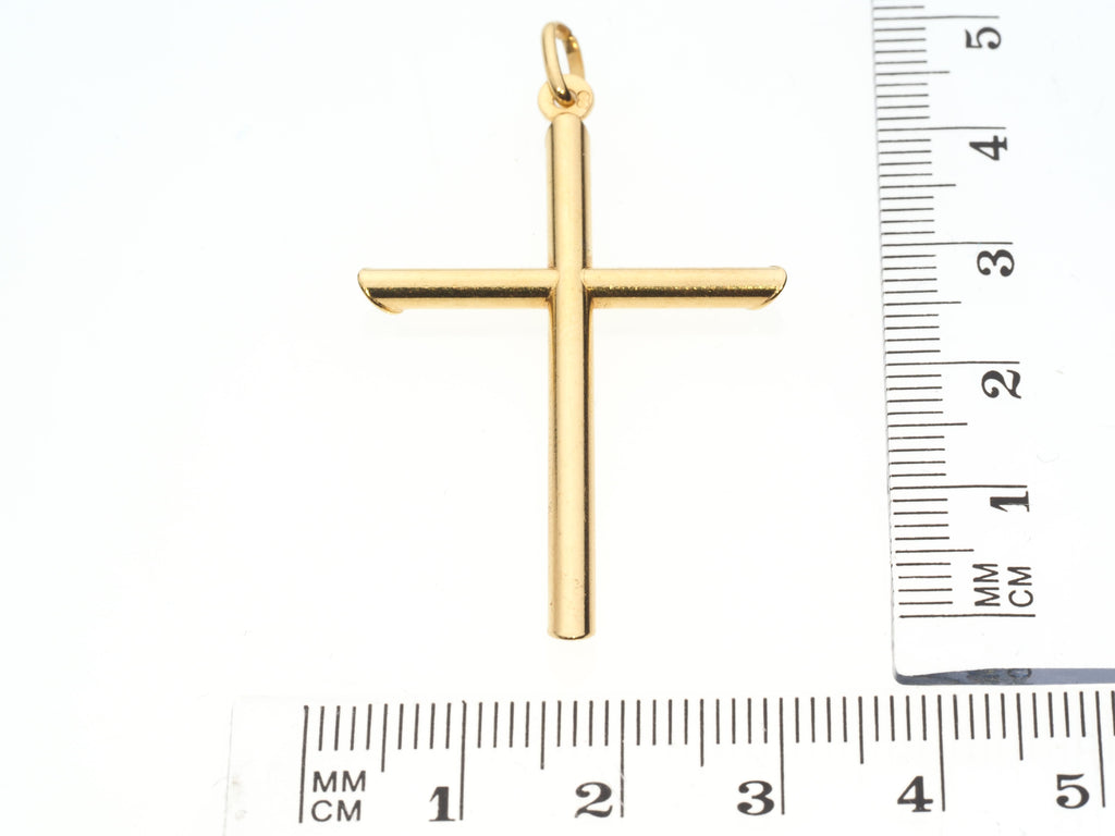 Gold cross pendant with a ruler for scale on a white background