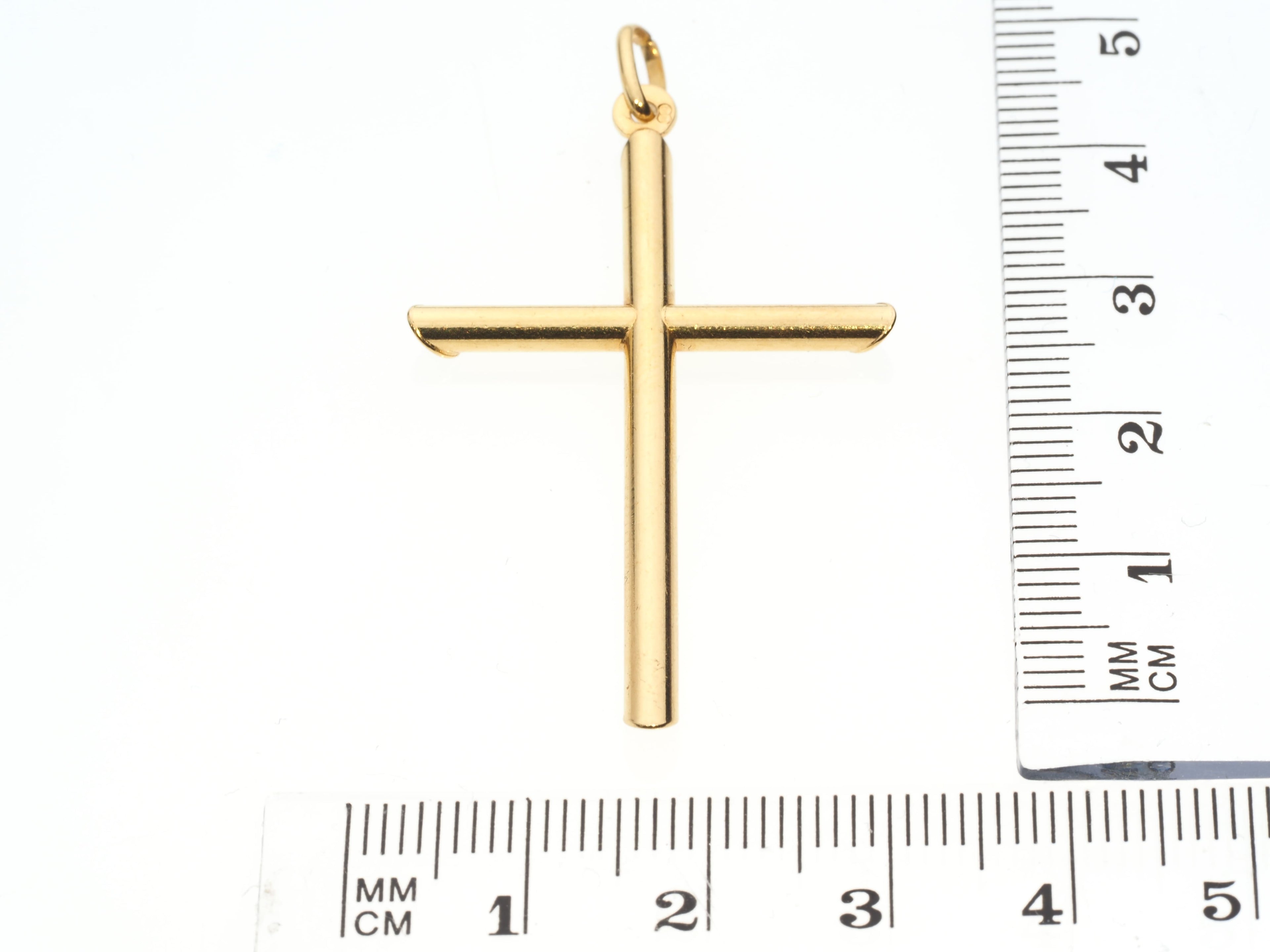Gold cross pendant with a ruler for scale on a white background