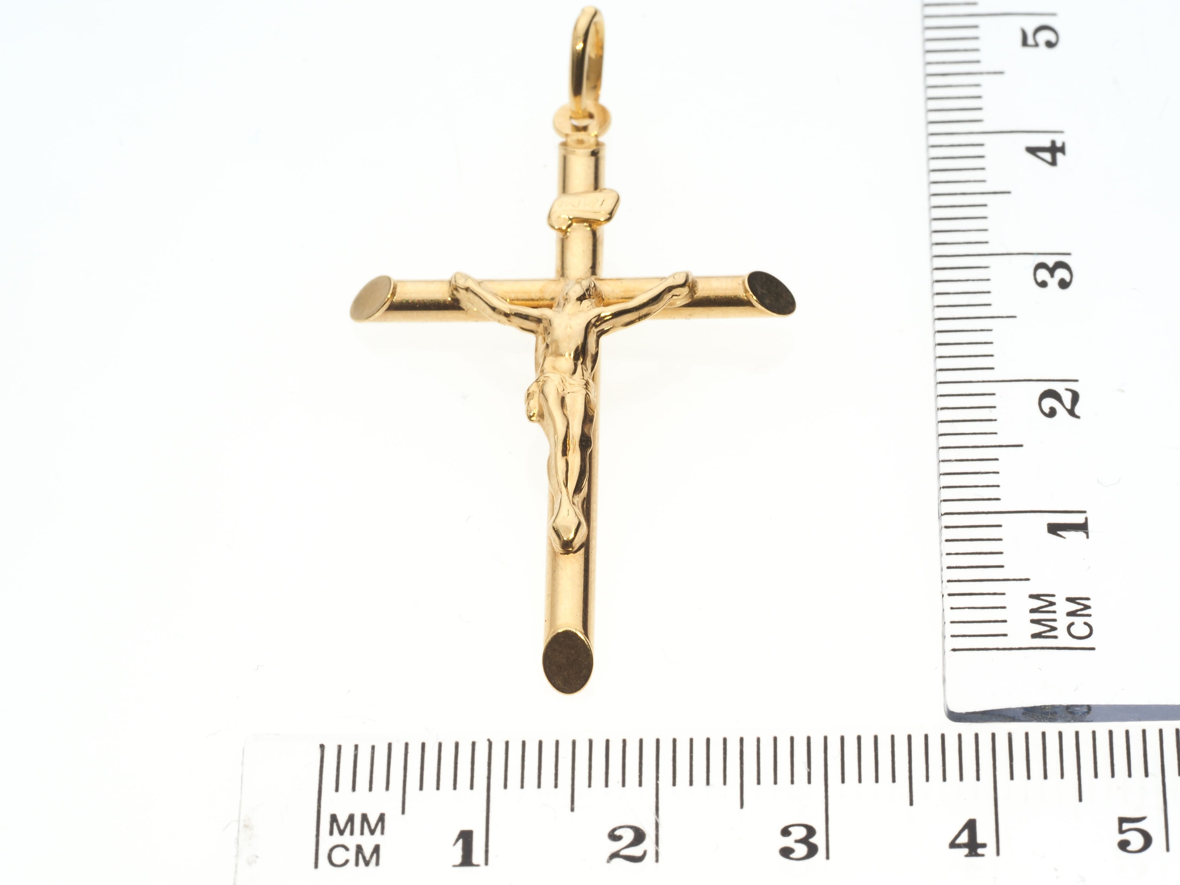 Gold crucifix pendant with a ruler for scale on a white background