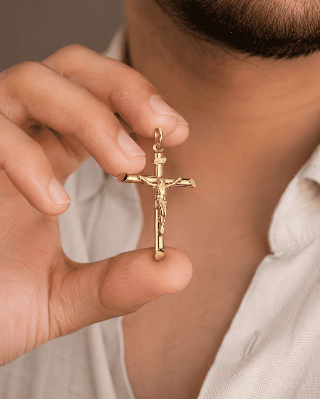 Gold crucifix pendant held by a hand against a neutral background