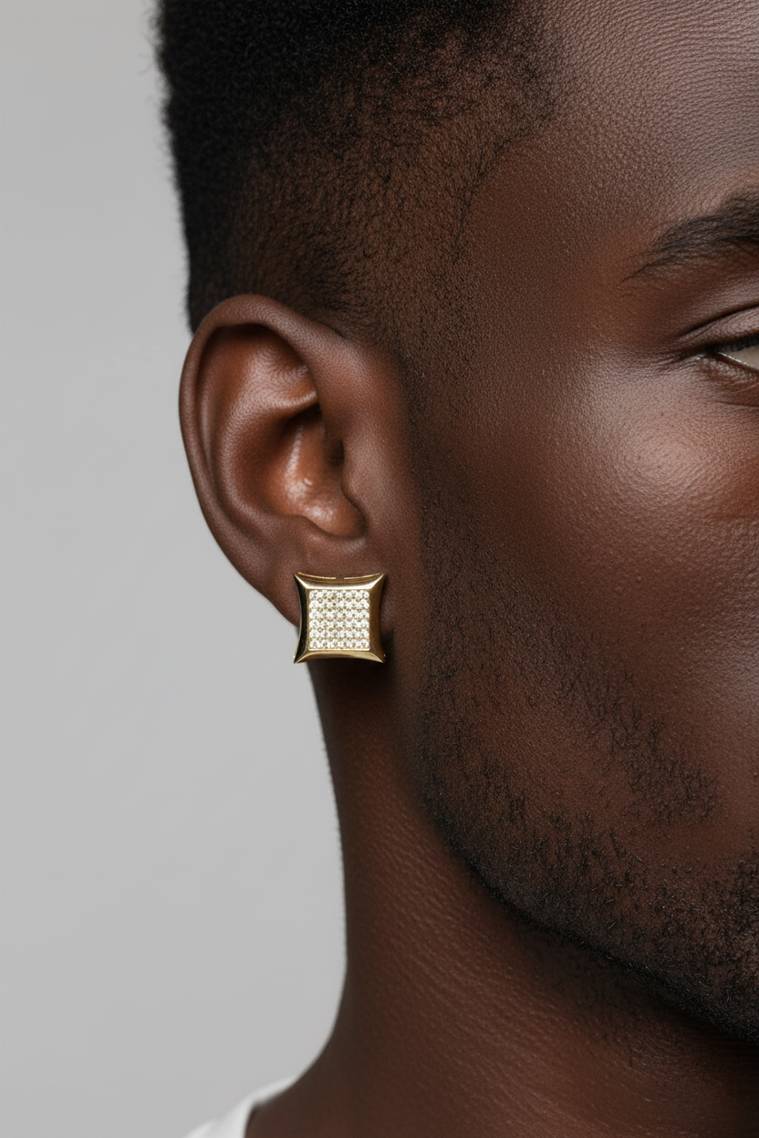 A close-up side profile of a man wearing a small square gold earring with a textured, diamond-like pattern on a light gray background.