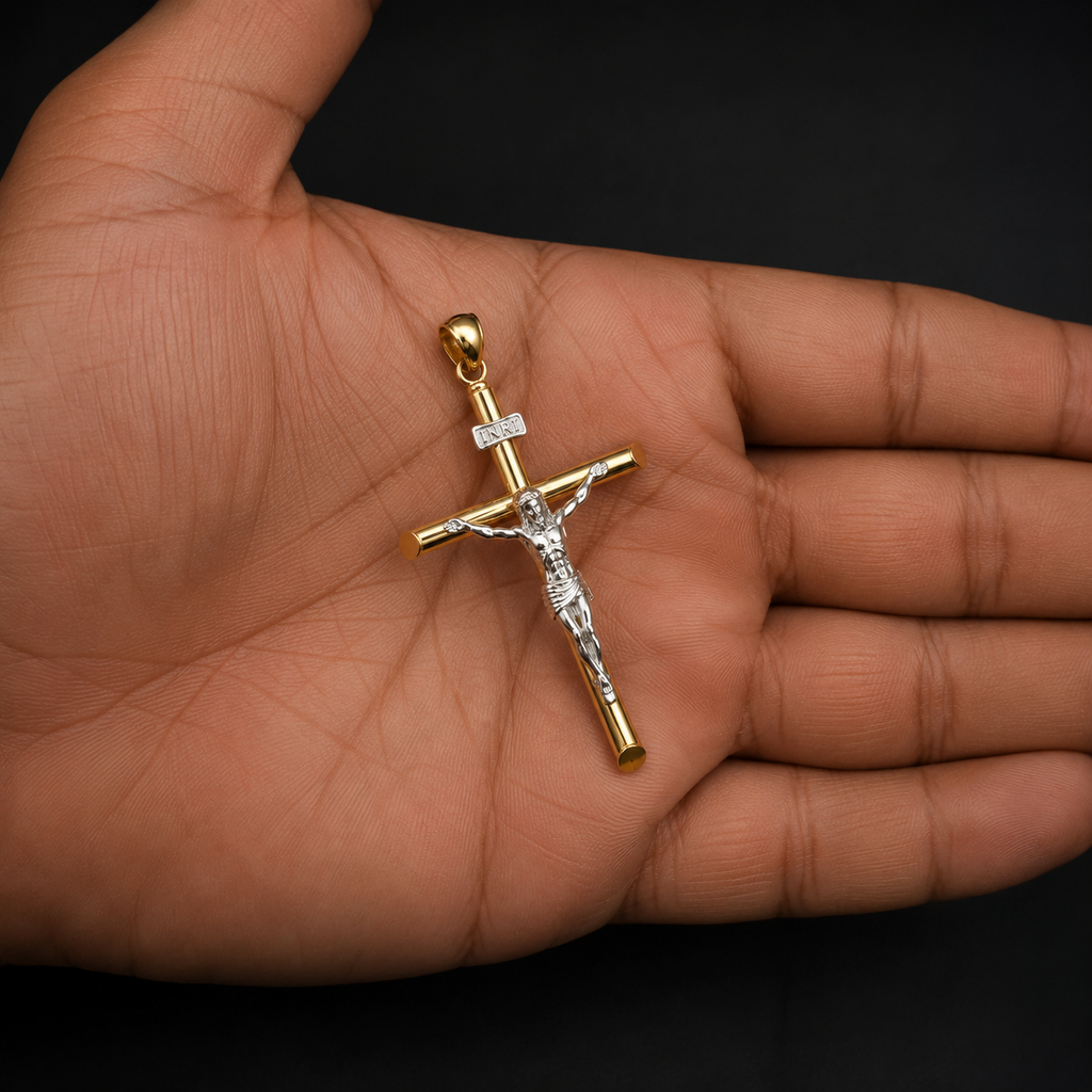 A gold and silver crucifix pendant with a clear central stone, held in the palm of a hand against a solid black background.