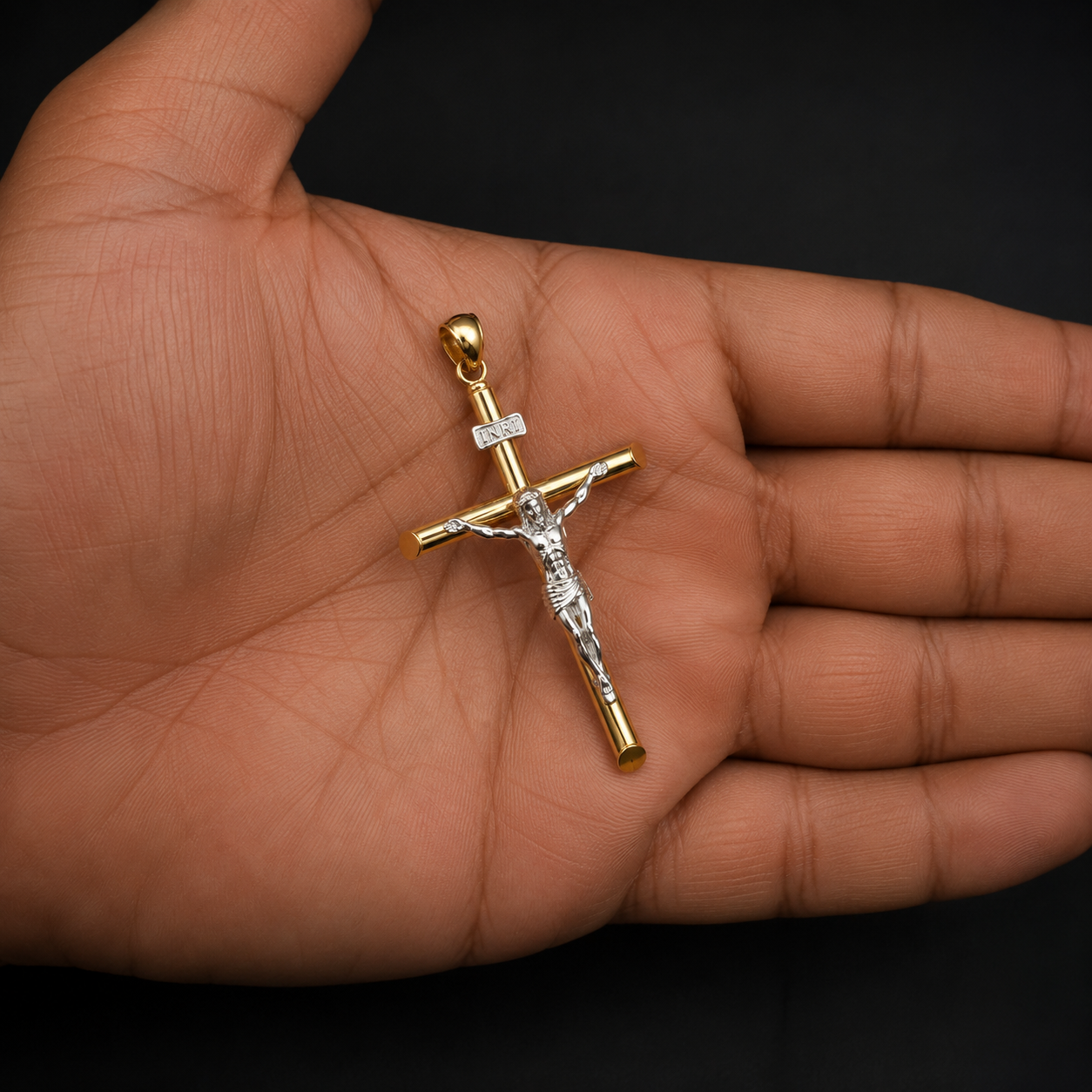 A gold and silver crucifix pendant with a clear central stone, held in the palm of a hand against a solid black background.