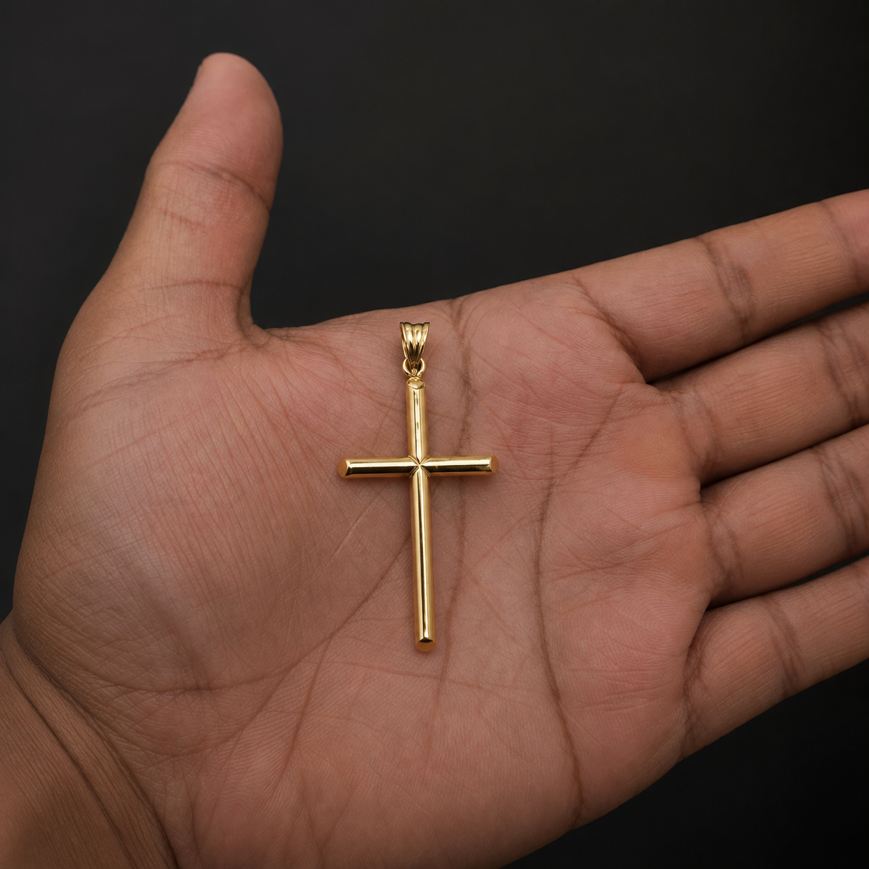 A polished yellow gold cross pendant with a bail, resting on the palm of a person's hand against a solid black background.