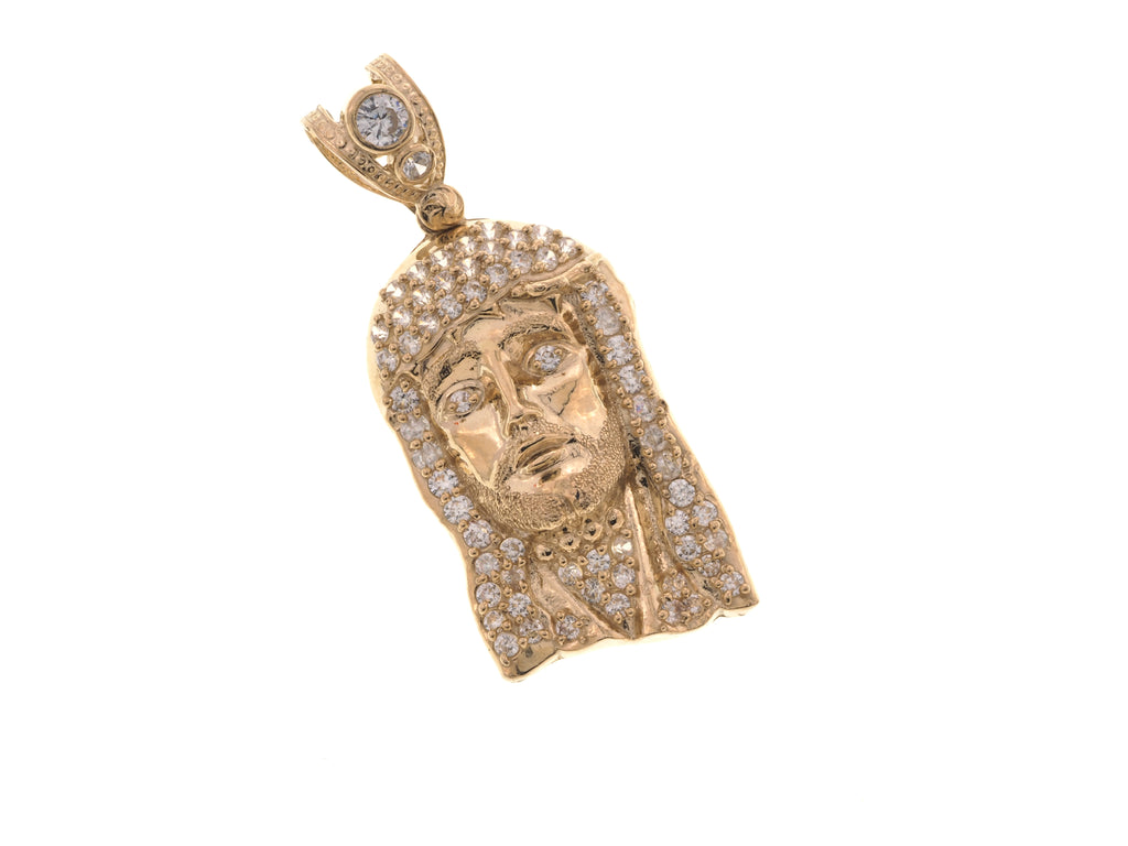 A gold pendant featuring a detailed face surrounded by pavé-set clear stones, with a matching stone in the bail, shown on a plain white background.