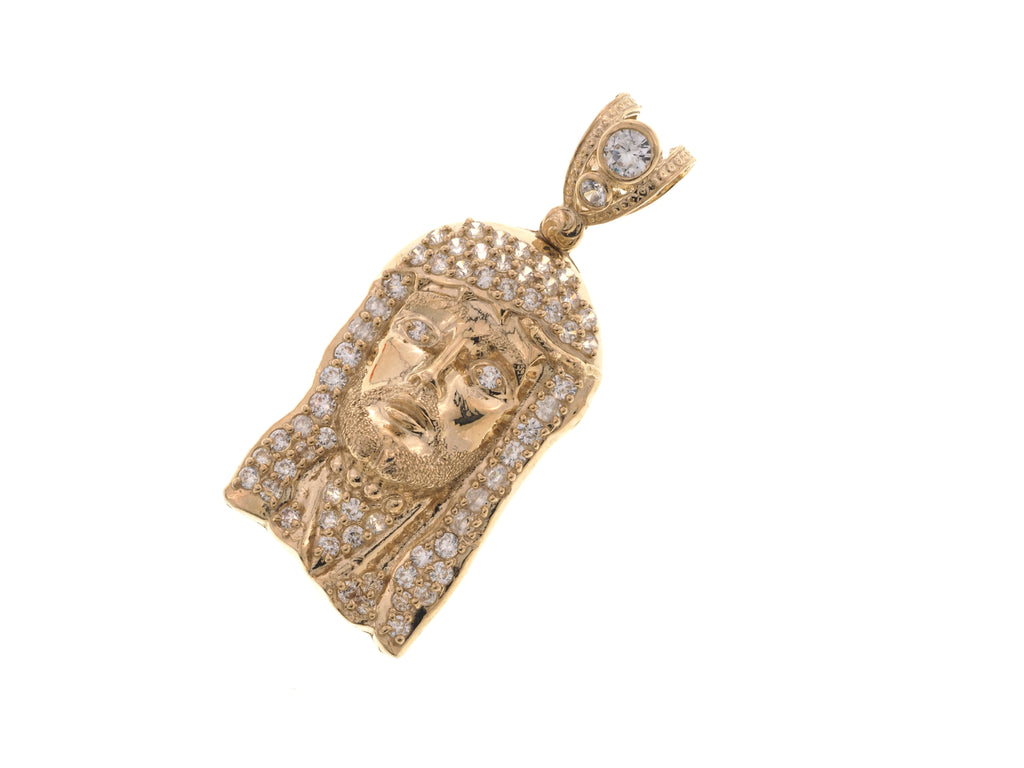 A gold pendant featuring a detailed face design, heavily embellished with small clear stones, shown on a plain white background.